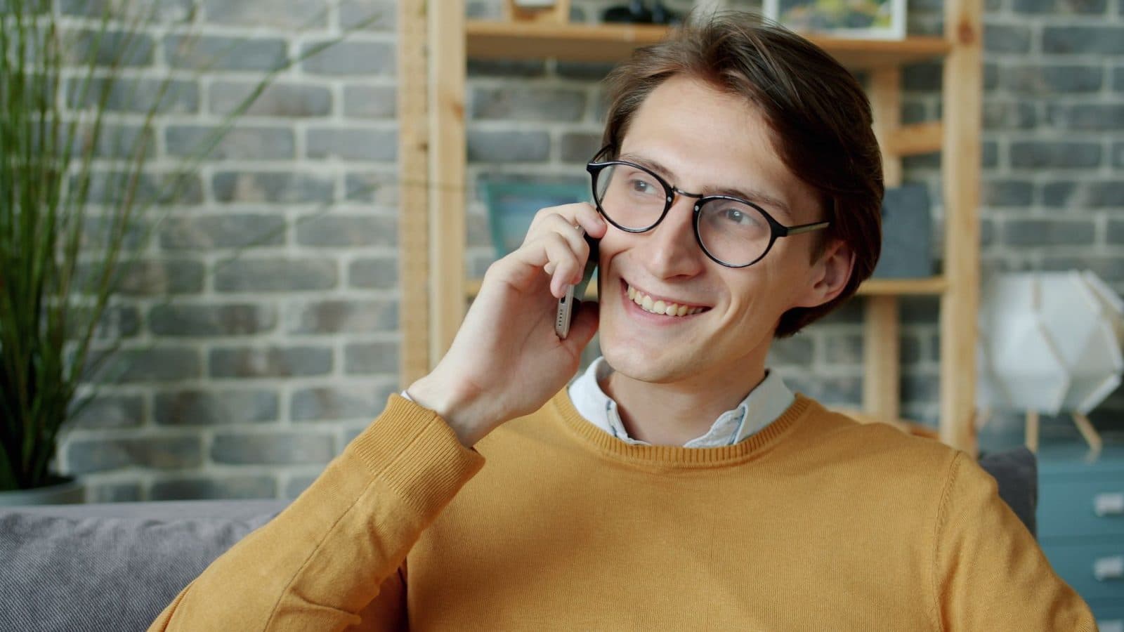 Smiling man in glasses talking on his phone at home