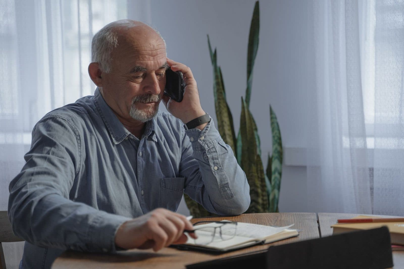 A man at home on a phone call, taking notes at his table