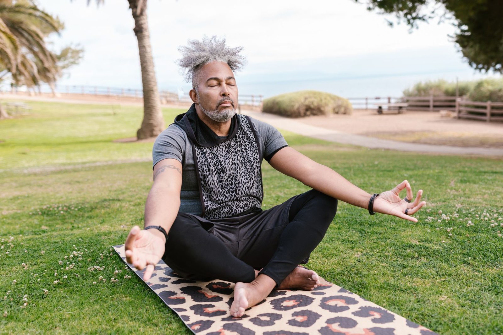 Older man breathing deeply while sitting cross-legged in a park