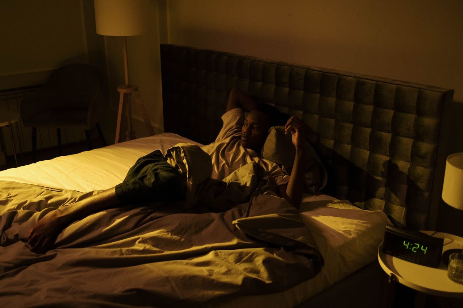 Man lying awake in bed at night next to a bedside clock