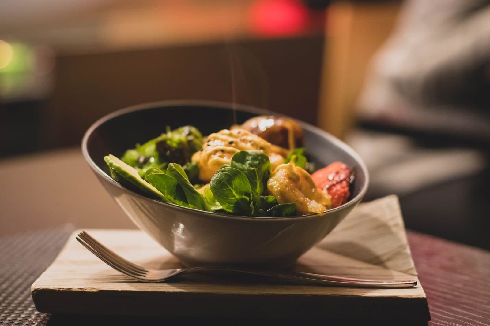 Bowl of leafy green salad with grilled chicken on a wooden board